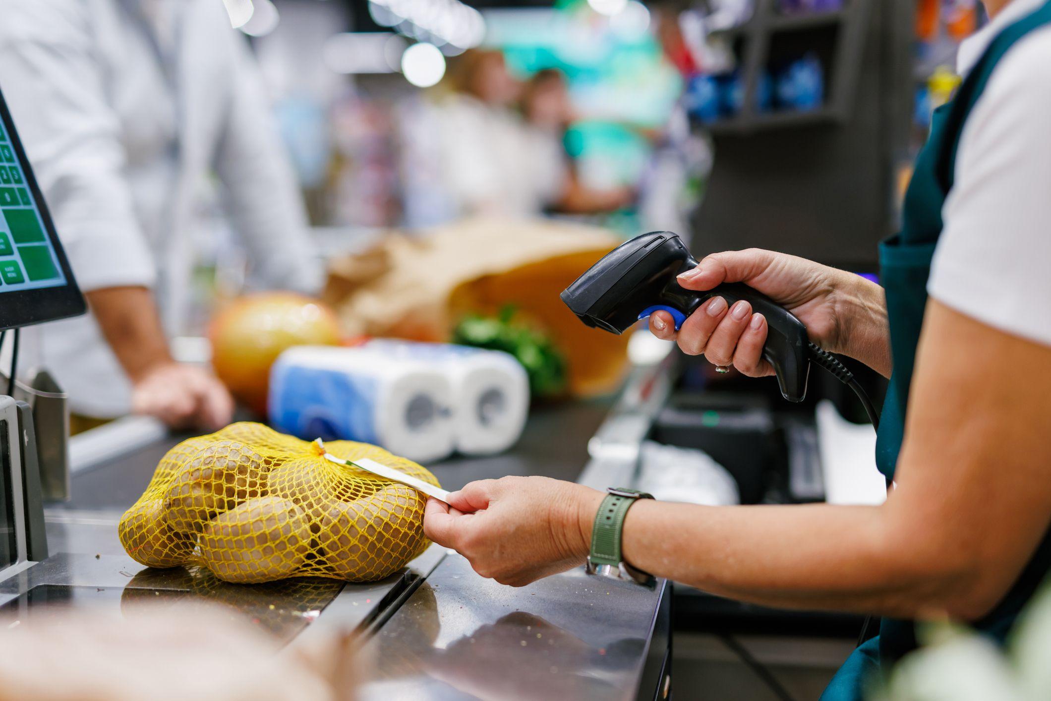 Operador de supermercado escaneando produtos no caixa com leitor de código de barras.